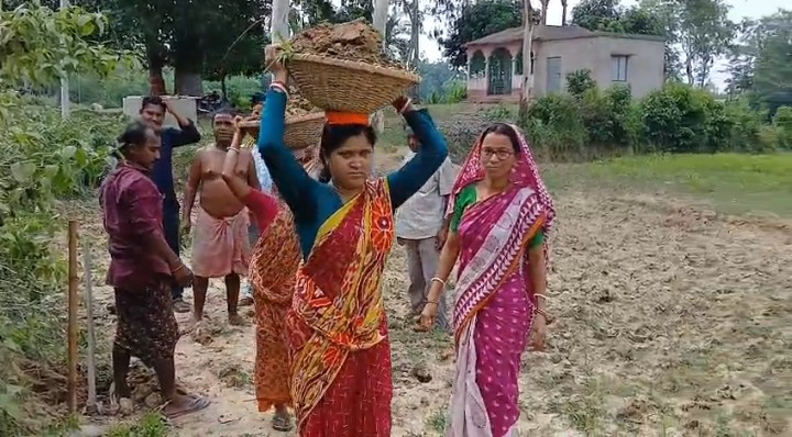 রাস্তা সংস্কারে মাটির ঝুড়ি মাথায় পঞ্চায়েত প্রধান। তৃণমূল বললো নাটক